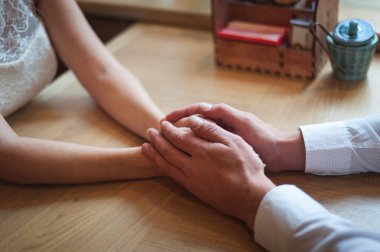 Birbirine aşık bir çift bir kafede el ele tutuşuyor. Ellere odaklan.