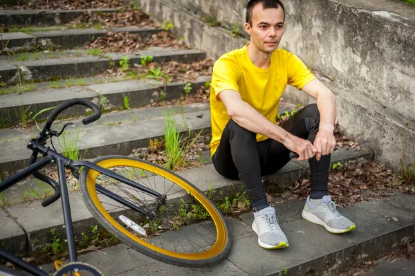 若い男が公共の公園で自転車で休むのをやめた 彼は森の中で早朝を楽しんでいる — ストック写真