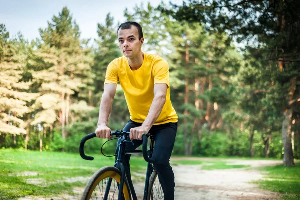 Portrait of a young man moving on a Bicycle. In a public Park, among trees and vegetation.