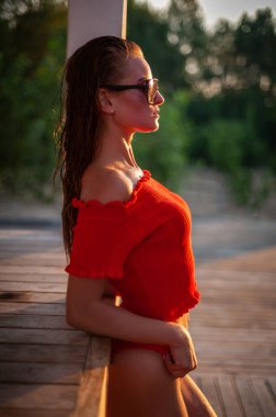 Kırmızı kazaklı ve siyah gözlüklü güzel esmer model kameranın önünde poz veriyor. Yakın çekim ve uzun menzilli çekim.