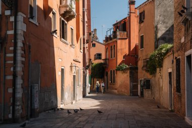 Venedik, İtalya - 13 Ağustos 2016: Turistler güneşli Venedik, İtalya 'nın dar ve parlak caddelerinde yürüyorlar.