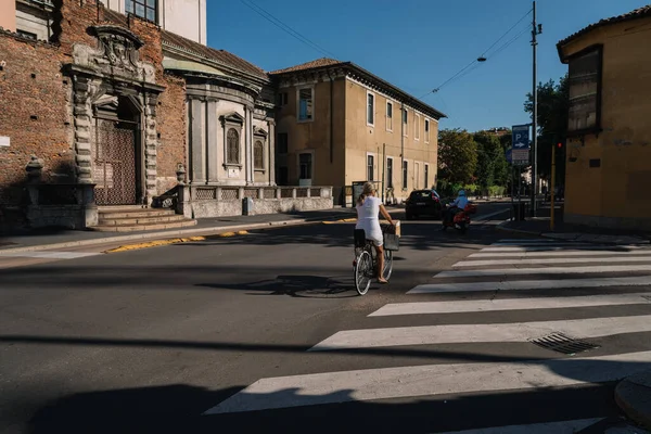 Milan, İtalya - 11 Ağustos 2016: Beyaz elbiseli İtalyan kadın, sabahleyin Milano, İtalya 'da güneşli bir sokakta çalışmak üzere bisiklet sürüyor.