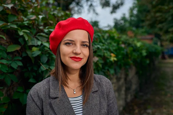 Kırmızı bere bir taş çit yakınındaki bir genç gülümseyen kadın portresi bitki örtüsü ile kaplı.