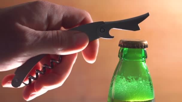 CLOSE UP: The Silhouette of Male hands opening brown beer bottle with opener. Opening cold bottle of beer with steam and spray slow motion — Stock Video