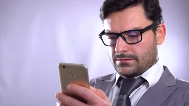 4k video footage of a young man using a cellphone against a grey background . Always in touch. Smiling young man holding smart phone and looking at it. Young happy smiling urban professional man using — Stock Video