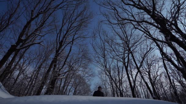 Περπατά όμορφος άνδρας σε ένα Χειμερινό μπουφάν και πουλόβερ. Όμορφη χιονώδη χειμερινή ημέρα άνθρωπος κάνει ένα ρυθμό πάνω από φωτογραφική μηχανή, στον ουρανό — Αρχείο Βίντεο