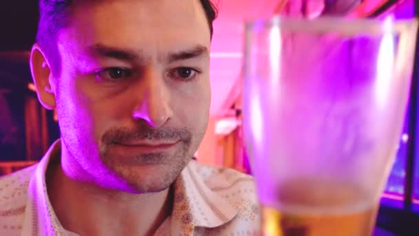 O retrato de homem bebendo cerveja escura fundo interior com luzes de néon fresco como gradientes de duotone roxo, azul e rosa — Vídeo de Stock