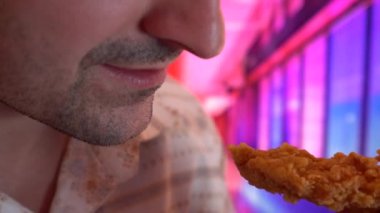 yakın çekim, adam yiyor, fast food, tavuk nuggets, kanatları ve patates kızartması modern interiorr gibi arka planda ile serin Neon ışıkları mor, mavi ve pembe çift tonlu degradeleri