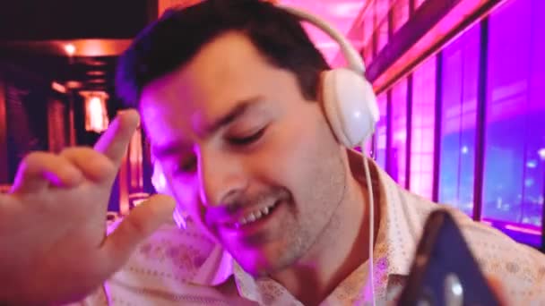 Joven hombre sonriente escuchando música con auriculares y bailando fondo interior aislado con Cool Neon Lights como gradientes de duotono púrpura, azul y rosa — Vídeos de Stock