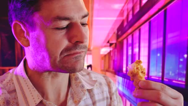 Eats fried chicken in a fast food background with Cool Neon Lights like purple, blue, and pink duotone gradients — Stock Video