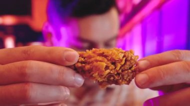 Genç adam yeme lezzetli ızgara tavuk kanat iç arka plan ile serin Neon ışıkları mor, mavi ve pembe çift tonlu degradeleri gibi gevrek fried chicken