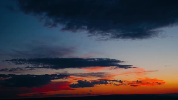 Dramatyczne chmury formatowania burzy w jasnych kolorach podczas zachodu słońca. Czerwony, pomarańczowy, Purpurowy Zachód słońca niebo z chmur, szybki ruch upływ czasu. Pochmurny zachód słońca nad wioską i górami — Wideo stockowe