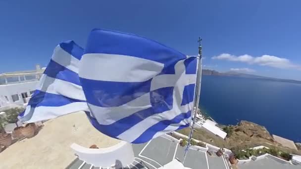 Bandera griega ondeando desde una iglesia en Oia, Santorini . — Vídeos de Stock