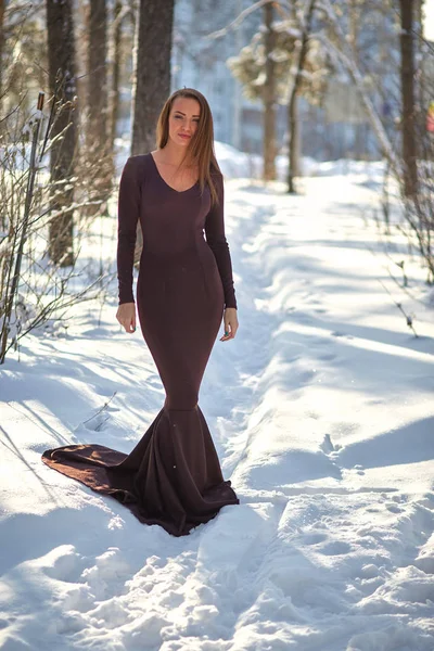 young woman in long dress on snow in winter forest