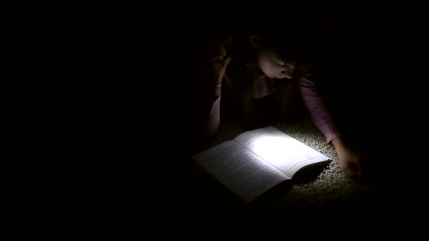 Holčička je čtení knihy s baterkou v tmavé místnosti v noci