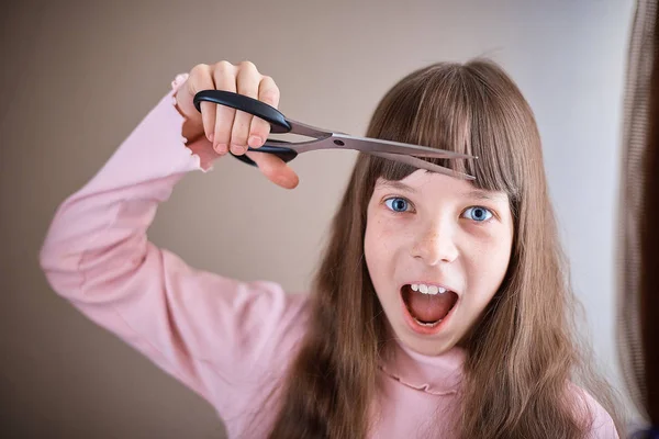 a little girl with freckles and blue eyes with scissors cuts her hair