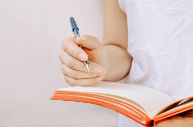 Beyaz bir arka plan üzerinde kalem ve kırmızı not defteri tutan kadın elleri. 