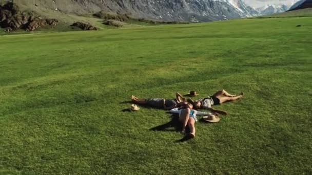 Drei attraktive Mädchen liegen auf grünem Gras und haben Spaß auf einer Wiese sonnigen Tag und Hintergrund der Berge — Stockvideo