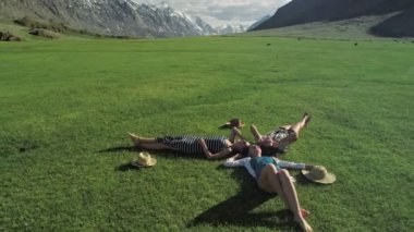 yeşil çim üzerinde yalan ve having fun bir çayır güneşli gün ve dağ arka plan üzerinde üç çekici kızlar