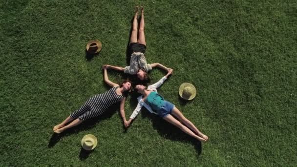 Tres chicas atractivas tumbadas sobre hierba verde y divirtiéndose en un prado día soleado y fondo de montaña — Vídeo de stock