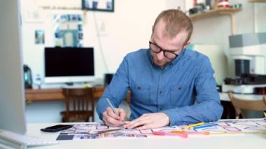 Hipster mühendis planı ile çalışır. Yukarıdan ateş. Ofiste çalışan genç mimari mühendis. Sakallı adam gözlüklü çizimler yapar. Loft style, minimalist iç, masanın üzerinde çizimler