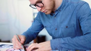 Hipster mühendis planı ile çalışır. Yukarıdan ateş. Ofiste çalışan genç mimari mühendis. Sakallı adam gözlüklü çizimler yapar. Loft style, minimalist iç, masanın üzerinde çizimler