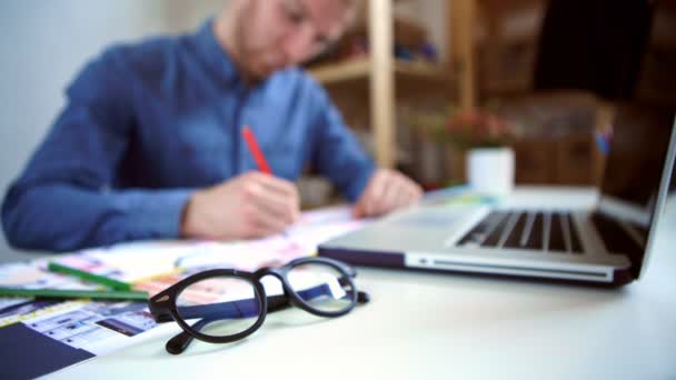 Hipster ingenieur werkt met blauwdruk. Schiet van boven. Jonge burgerlijk ingenieur-architect werkzaam in kantoor. Bebaarde man in glazen maakt schetsen. Loft stijl, minimalistische interieur, tekeningen op tafel — Stockvideo