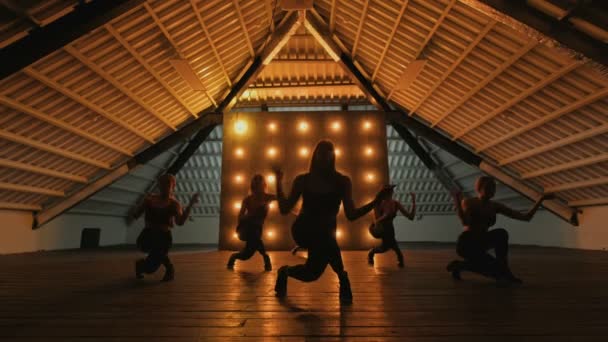 Silhuetas de meninas dançarinas. Dança de go-go. Desempenho de dança close-up de grupo feminino bonito em um palco escuro com luzes amarelas. dança de equipe de mulheres de salto alto — Vídeo de Stock