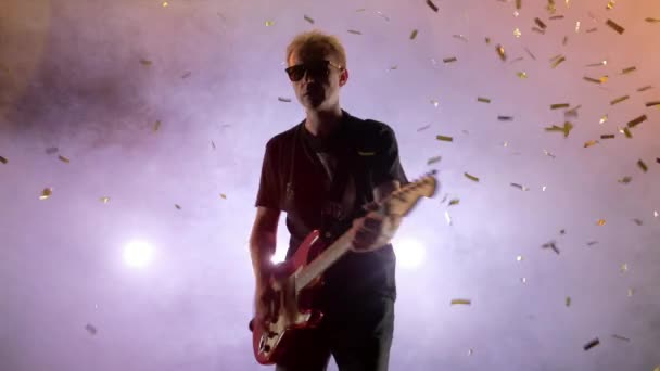 The guitarist performs on stage. Stage light, smoke. From above fall golden confetti — Stock Video