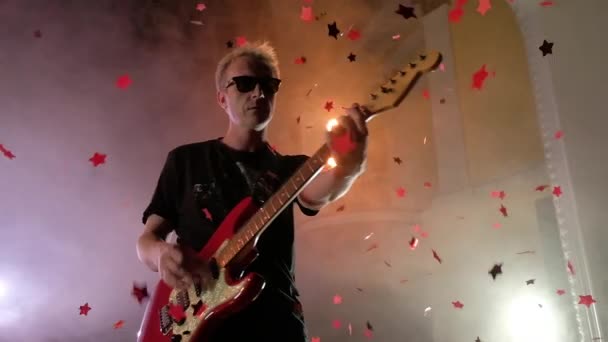 O guitarrista se apresenta no palco. Luz de palco, fumo. De cima caem confetes dourados — Vídeo de Stock