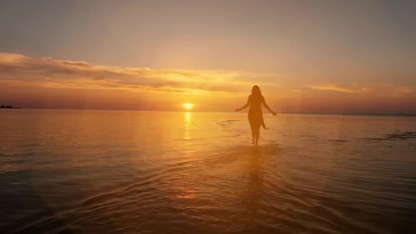 Mujer morena en un vestido corriendo a lo largo del agua al atardecer o al amanecer . — Vídeos de Stock