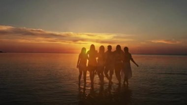 Grup beş mutlu insan boş günbatımı plaj arka plan üzerinde oturur. Seyahat veya deniz tatil kavramı