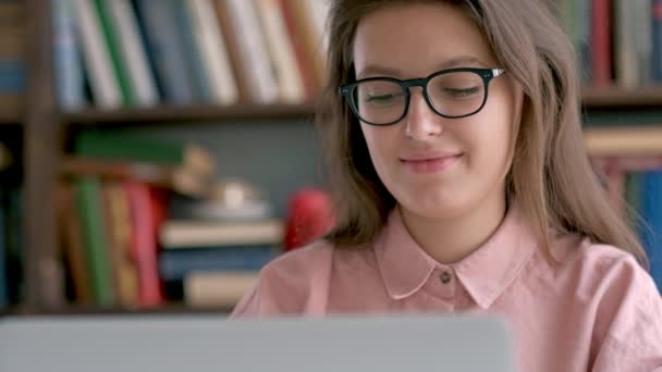 Studentka sedí proti Knihovnička a použití přenosného počítače v knihovně — Stock video