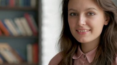 Kamera kitaplık kitaplık arka plan bilgi edinmekle mutlu bakarak gülümseyen genç güzel kütüphaneci kadın portresi kapatın