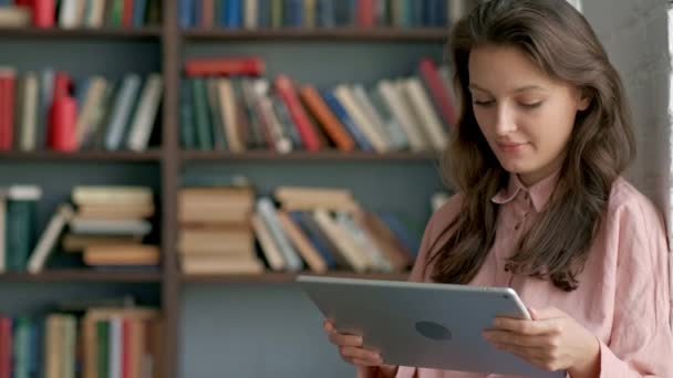 Χαριτωμένος νεαρός φοιτητής χρησιμοποιώντας έναν υπολογιστή tablet σε μια βιβλιοθήκη — Αρχείο Βίντεο