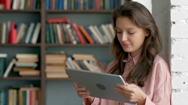 Estudante jovem bonito usando um computador tablet em uma biblioteca — Vídeo de Stock