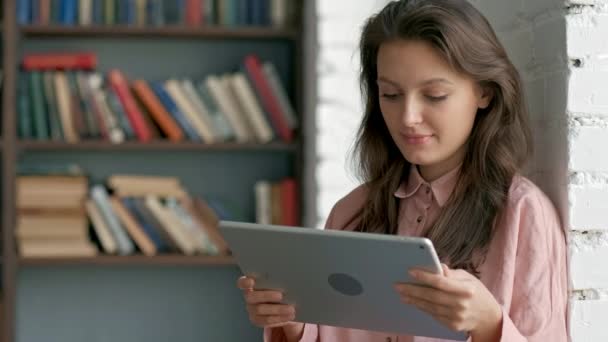 Lindo joven estudiante usando una tableta en una biblioteca — Vídeos de Stock