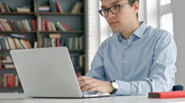 Sınav hazırlayan ve okul kütüphanesinde öğrenim dersleri alan öğrenci, dizüstü bilgisayarda araştırma yapıyor ve internette geziniyor.