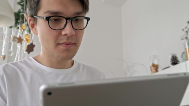 Hombre atractivo en casa usando tableta en la cocina enviando un mensaje en las redes sociales sonriendo disfrutando de un estilo de vida moderno usando camisa blanca — Vídeo de stock