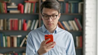 Genç adam portre ayakta Kütüphane sosyal medyada komik gülüyor smartphone kullanarak