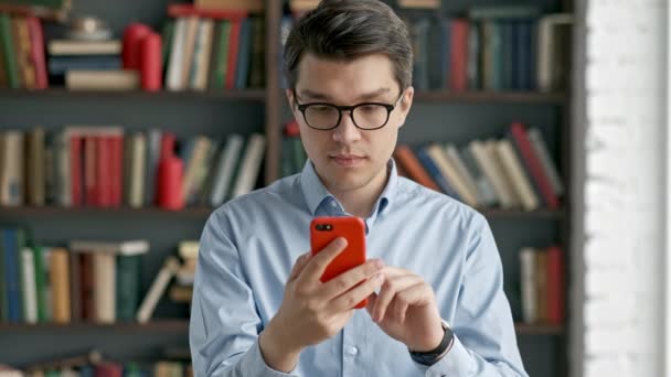 Retrato de hombre joven usando teléfono inteligente riendo de pie en las redes sociales biblioteca divertido — Vídeo de stock