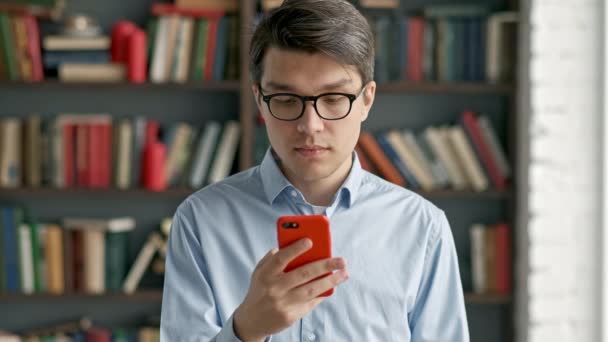 Retrato de hombre joven usando teléfono inteligente riendo de pie en las redes sociales biblioteca divertido — Vídeo de stock