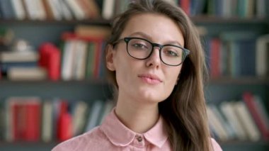 Kamera kitaplık kitaplık arka plan bilgi edinmekle mutlu bakarak gülümseyen genç güzel kütüphaneci kadın portresi kapatın