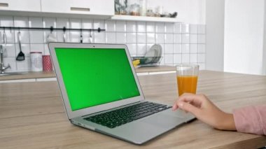 Çekici genç kadın laptop kullanıyor, modern mutfak, kadın yeme elma bilgisayar ekranında, ışık dairesinde duran sevimli gülümseme ile yeşil meyve ısırma arıyor. Kavram: iç