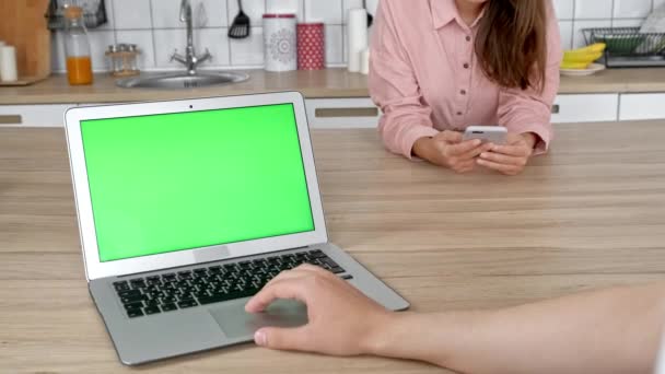 Jovem casal feliz usando laptop na cozinha antes de tomar café da manhã juntos pela manhã, sorrindo homem e mulher olhando para a tela do computador verificando as últimas notícias on-line em redes sociais — Vídeo de Stock