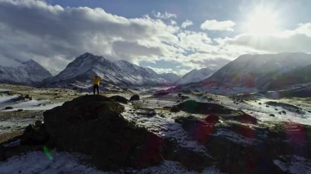 L'alpinista solitario si riposa sulla montagna innevata sopra le nuvole al sole, l'alpinista raggiunge la cima di una montagna innevata in una giornata invernale soleggiata. . — Video Stock