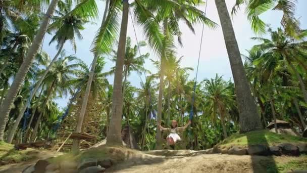 En flicka gungor på en gunga och ser solnedgången på en tropisk havsstrand. Frihet, vila, semester, resor koncept — Stockvideo