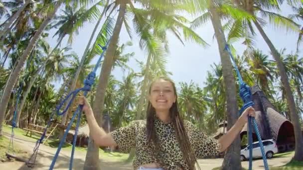 Uma menina balança em um balanço e olha para o pôr do sol em uma praia tropical. Liberdade, descanso, férias, conceito de viagem — Vídeo de Stock