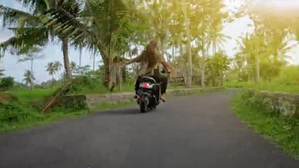 Pareja feliz tropezando en motocicleta en carretera tropical al atardecer. Foto al aire libre de una joven pareja montando en moto. Hombre montando en una motocicleta con su novia en el camino rural . — Vídeos de Stock