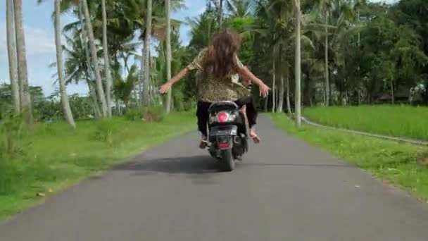 Casal feliz tropeçando de moto na estrada tropical ao pôr do sol. Tiro ao ar livre de jovem casal andando de moto. Homem montando em uma motocicleta com namorada na estrada rural . — Vídeo de Stock